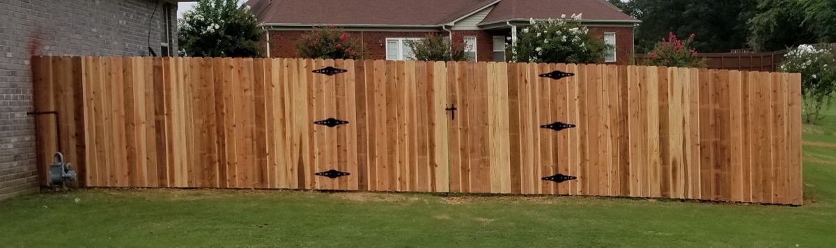 Wide cedar fence with multiple gates and decorative iron hardware on green lawn