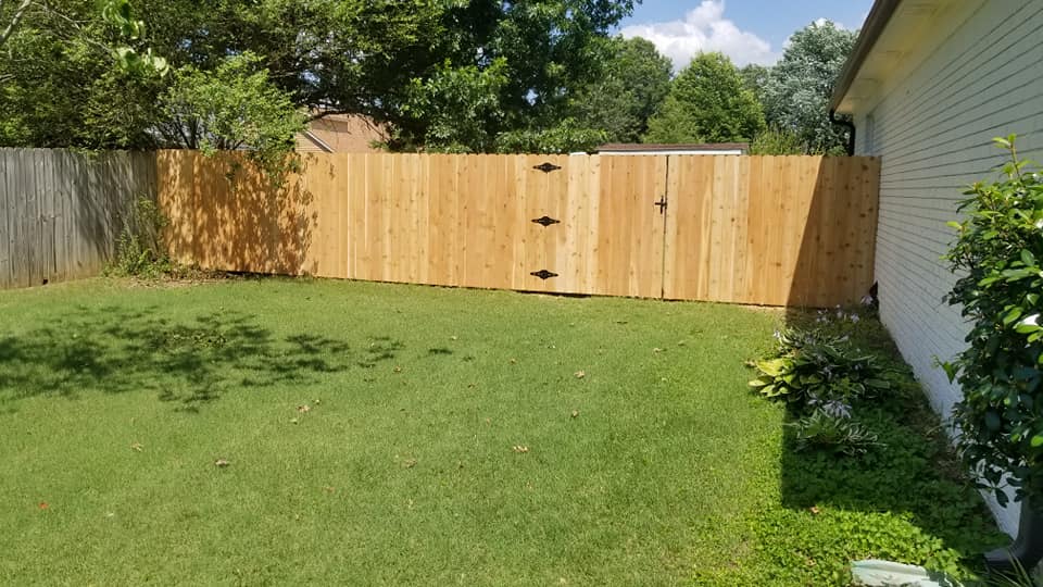 Wood privacy fence and gate with decorative hardware on green lawn