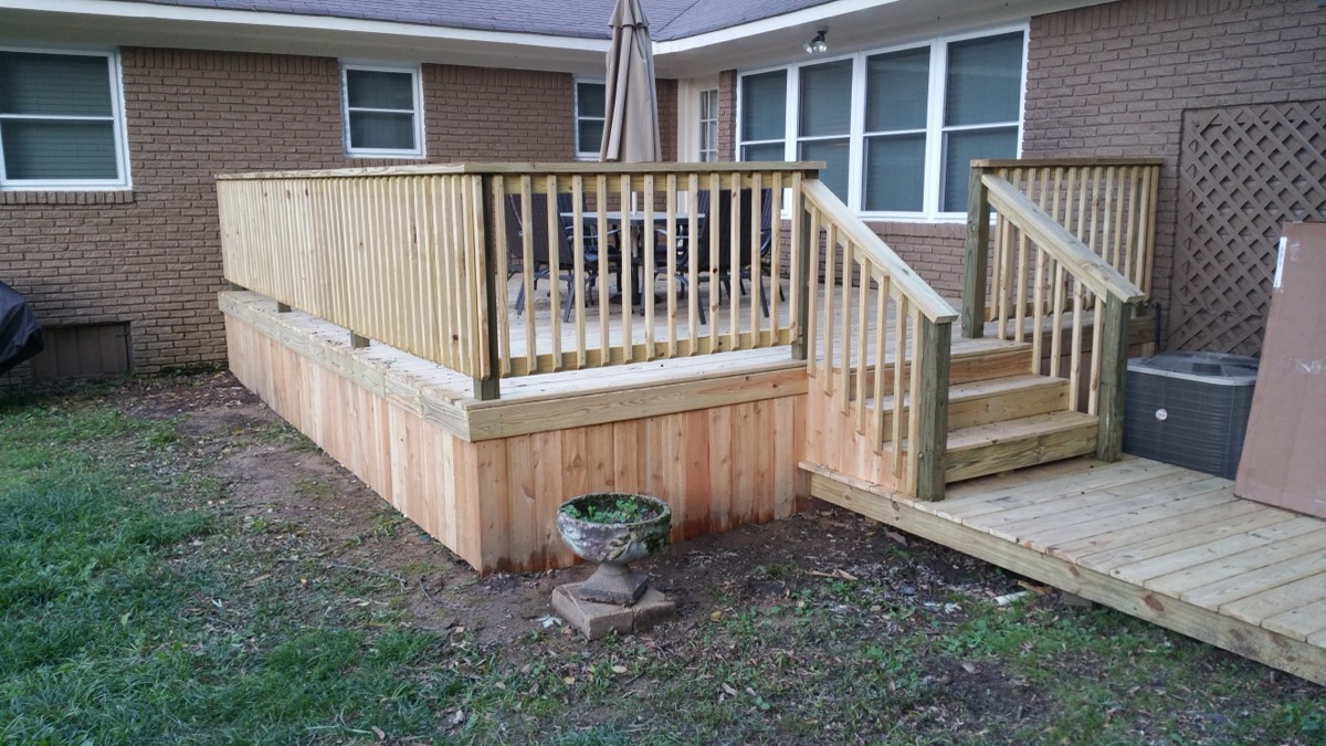 Custom wood deck with railing and stairs beside brick house