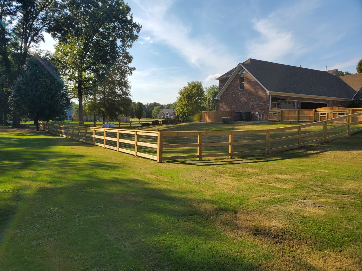 Ranch-style rail fence around large residential property at sunset
