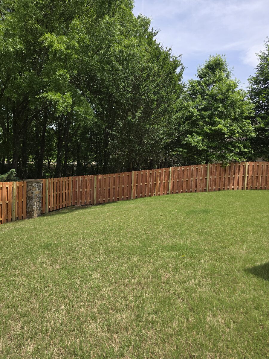 Shadowbox fence curving around large backyard with stone column accent