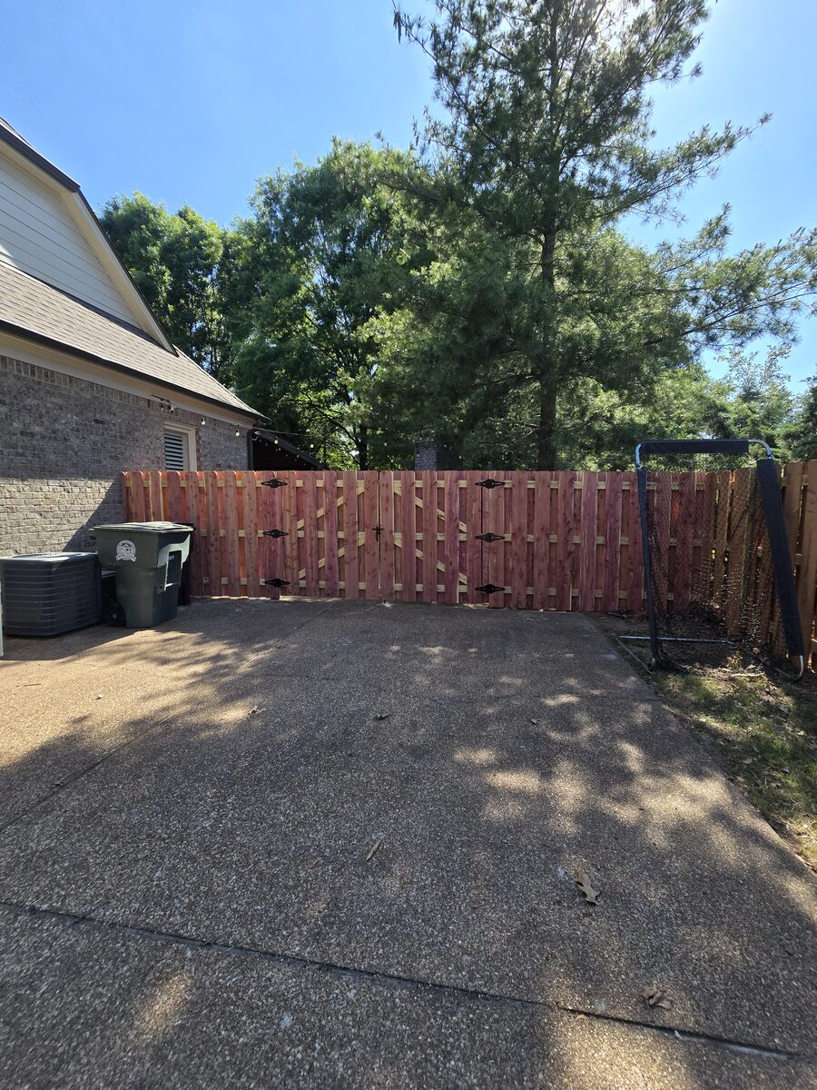 Shadowbox double gate with black hardware across concrete driveway