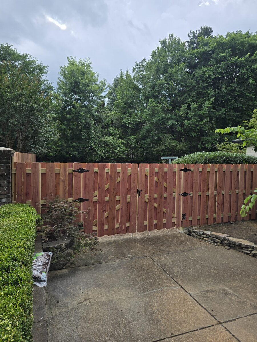Shadowbox double gate with decorative hinges beside landscaped patio
