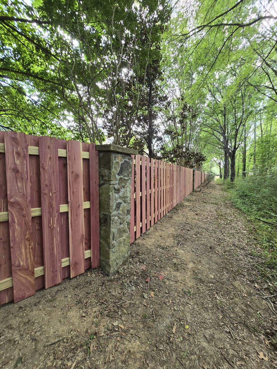 Red cedar shadowbox fence with stone columns along wooded path