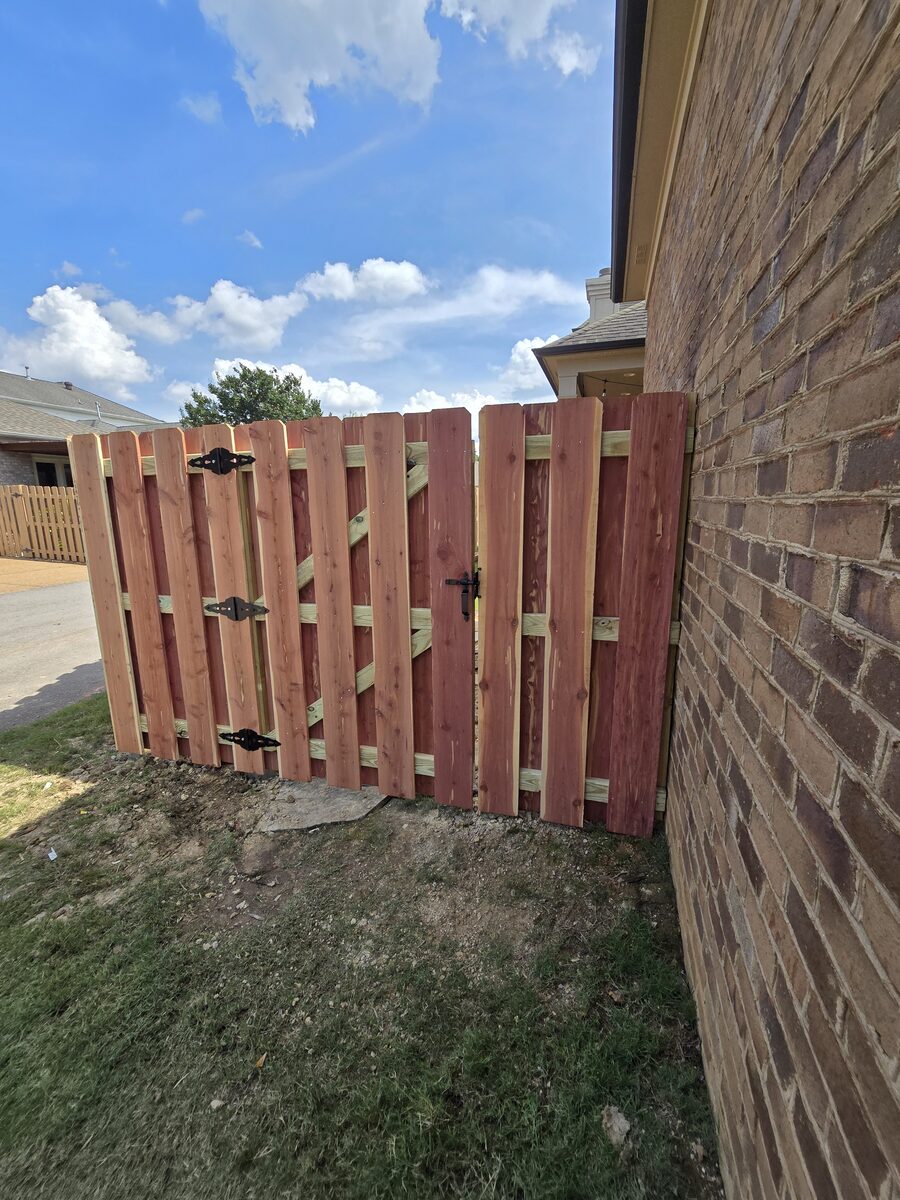 Cedar shadowbox walk gate with black hardware beside brick house